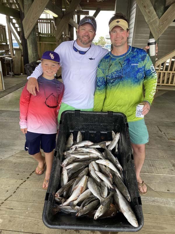 Three men are standing next to each other holding a bucket of fish.