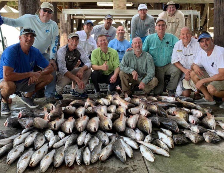 A group of men are posing for a picture with a pile of fish.