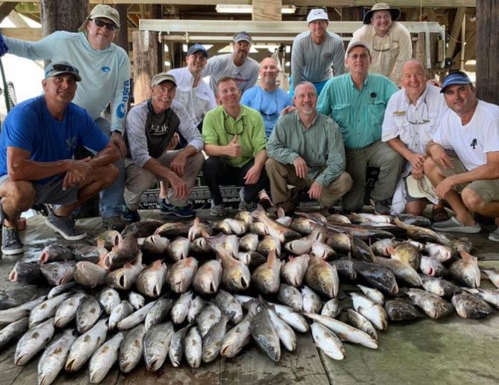 A group of men are posing for a picture with a pile of fish.