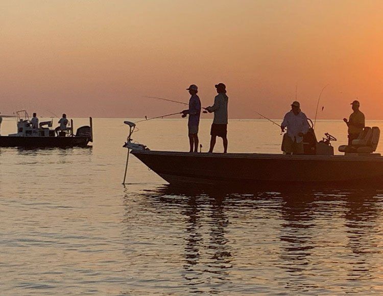 A group of people are fishing from a boat in the ocean at sunset.