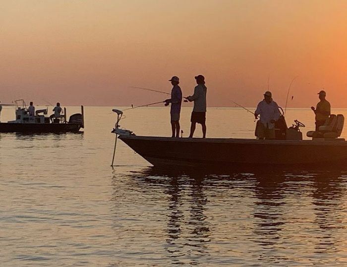 A group of people are fishing from a boat in the ocean at sunset.