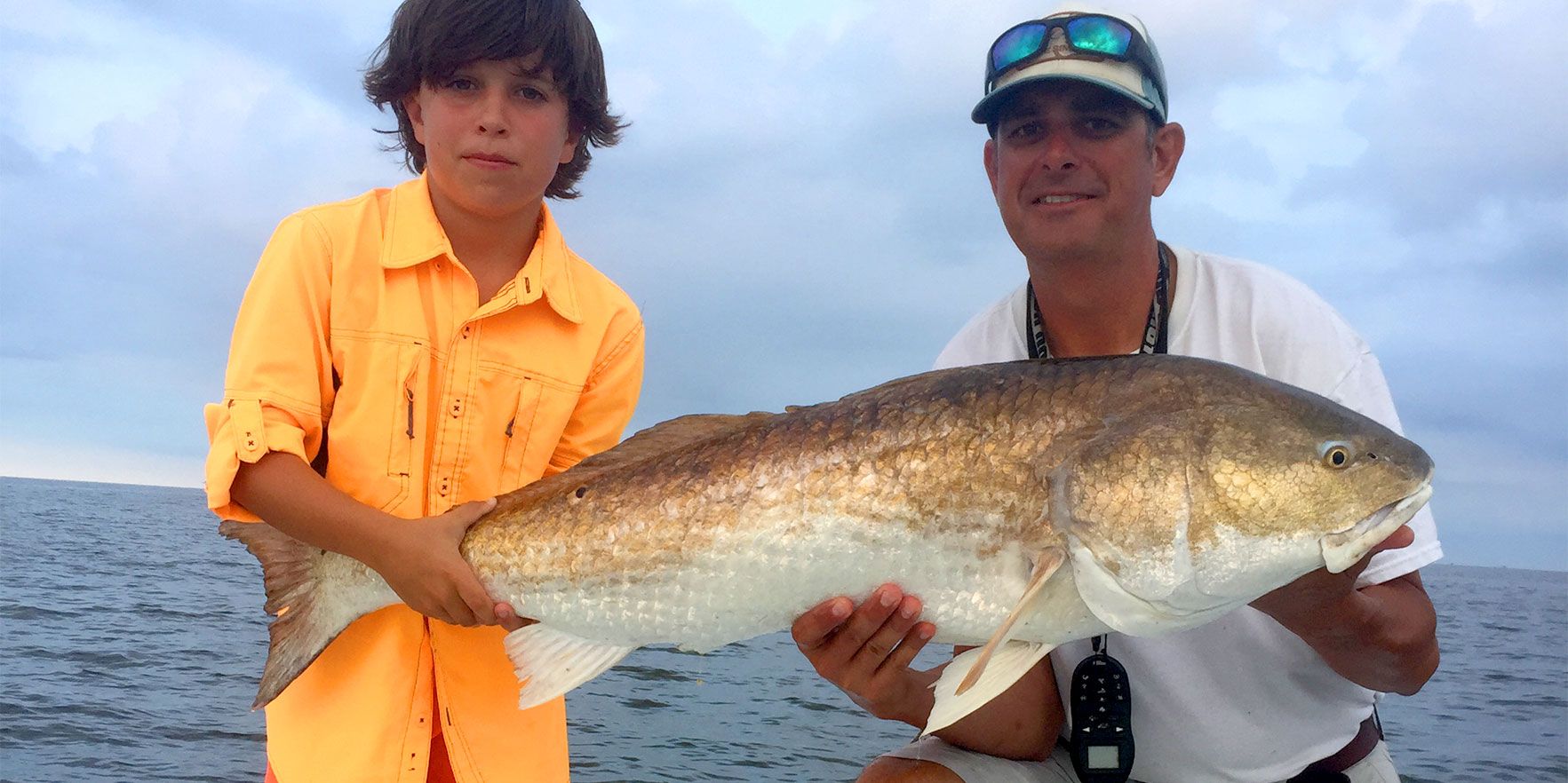 A man and a boy are holding a large fish on a boat.