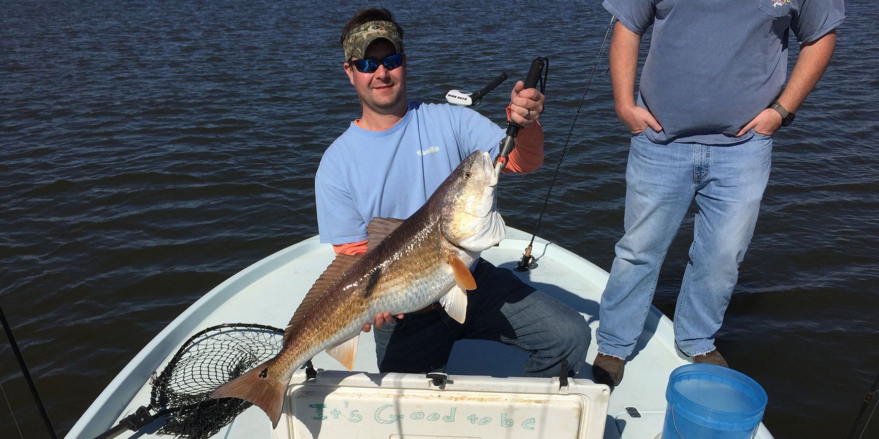 Two men are standing on a boat holding a large fish.