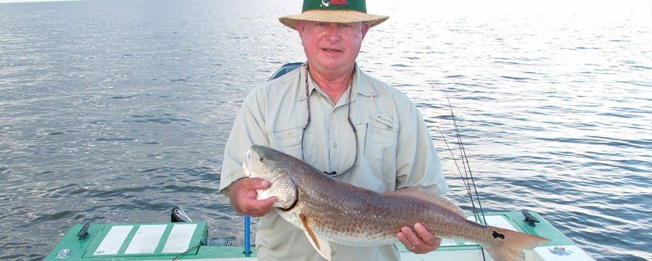 A man in a hat is holding a large fish in his hands.