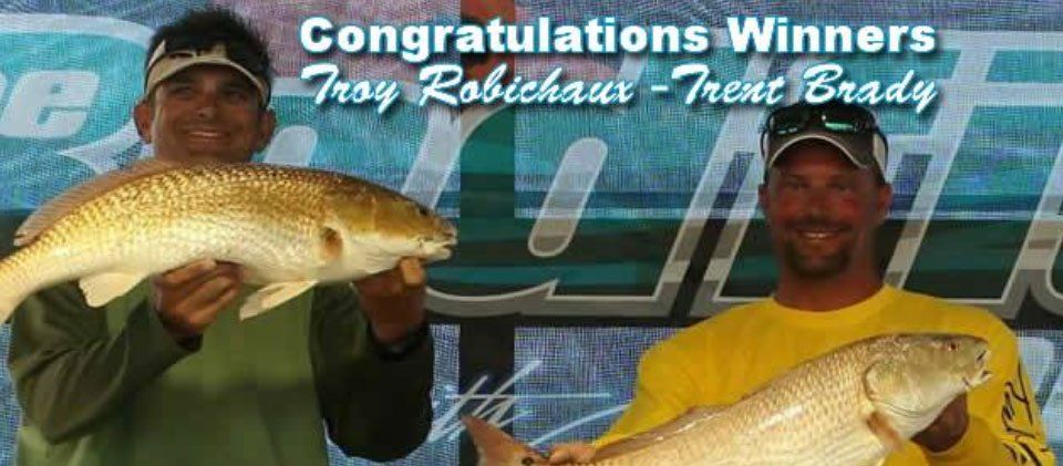 Two men holding fish in front of a sign that says congratulations winners