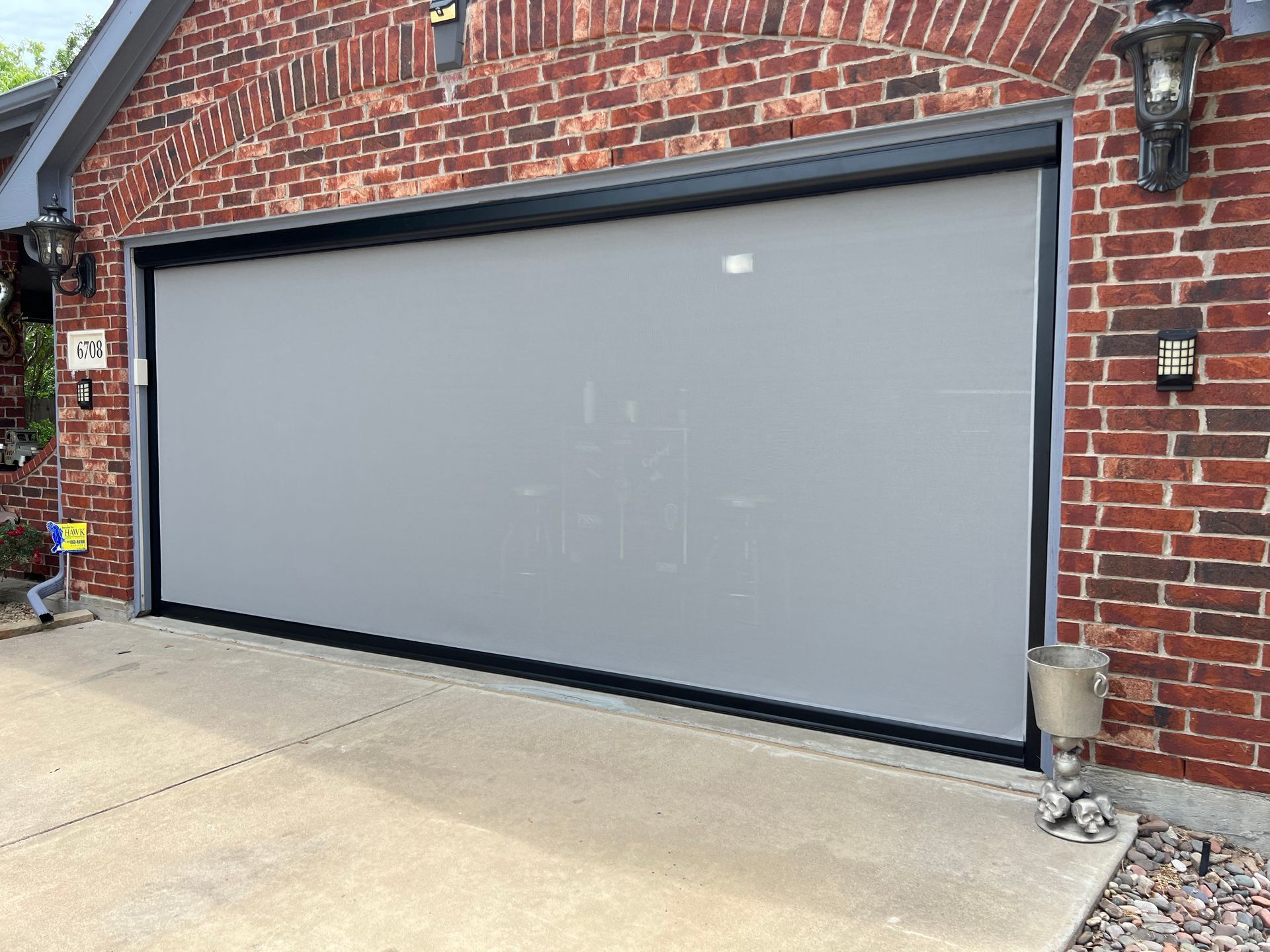 A gray garage door is sitting in front of a brick house.