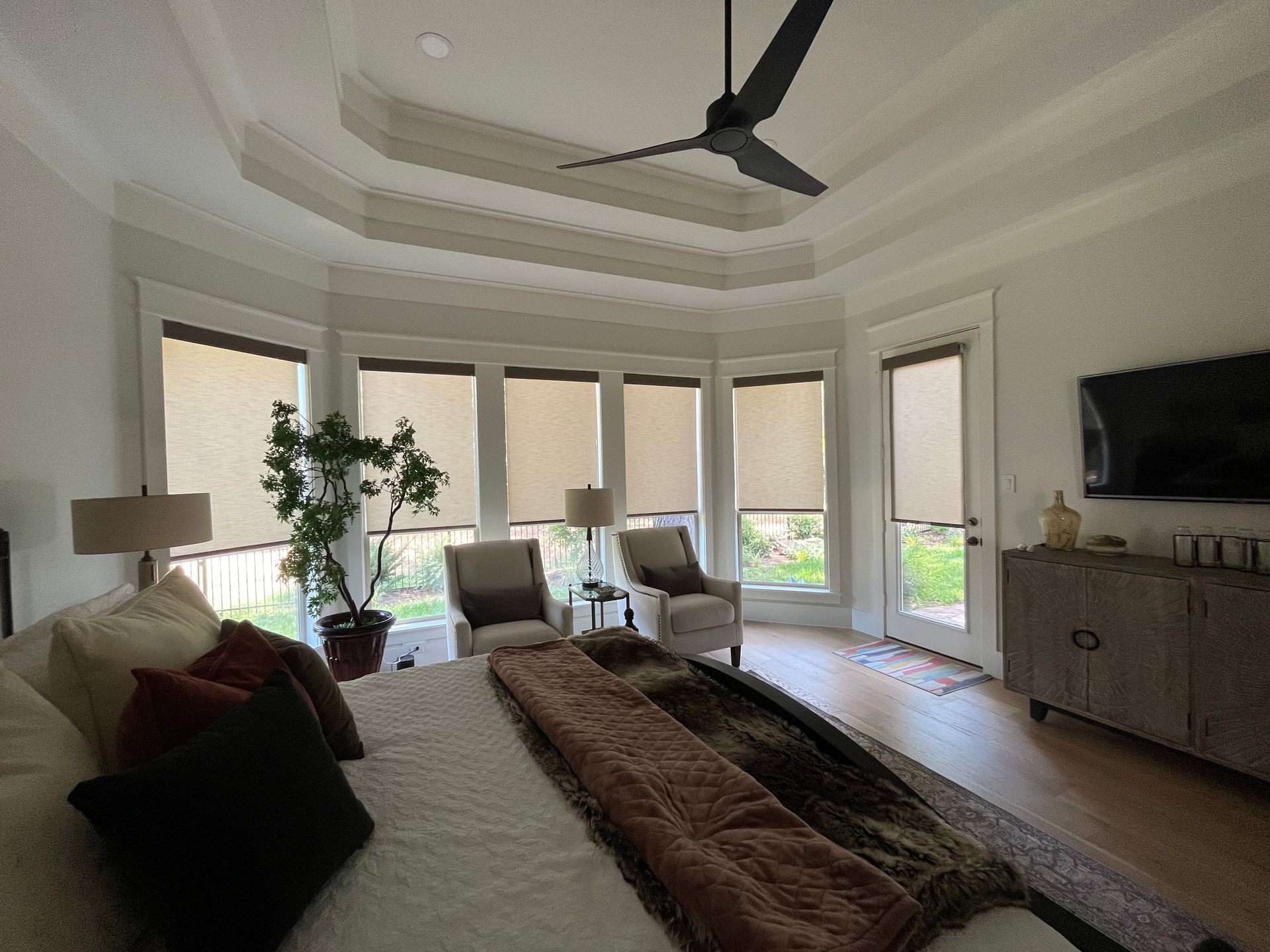 A bedroom with a large bed , chairs , a television and a ceiling fan.