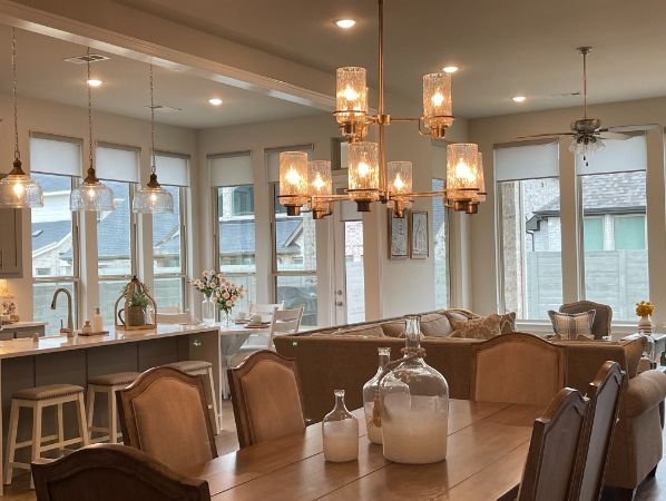 An elegant dining room with a dining table and chandelier sits in a room with many windows with roller shades.