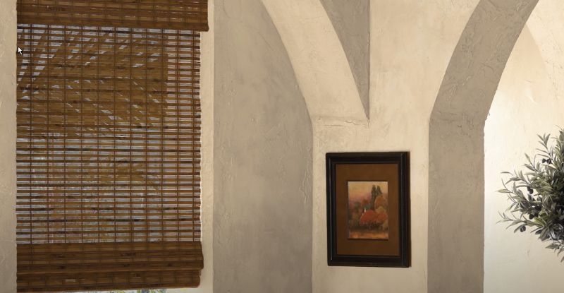 Woven wood blinds decorate a window in a corner with a picture and a plant.