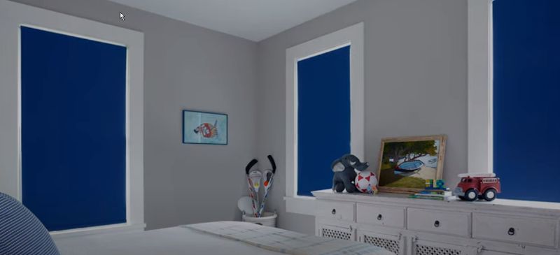 A bedroom with bright blue roller shades has the shades closed. 