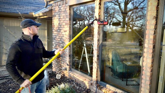 A man is cleaning a window with a pole.