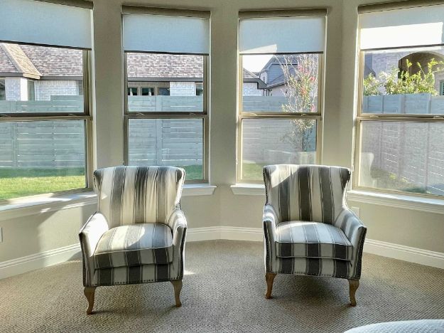 A sitting area with two chars has a bay window with roller shades.