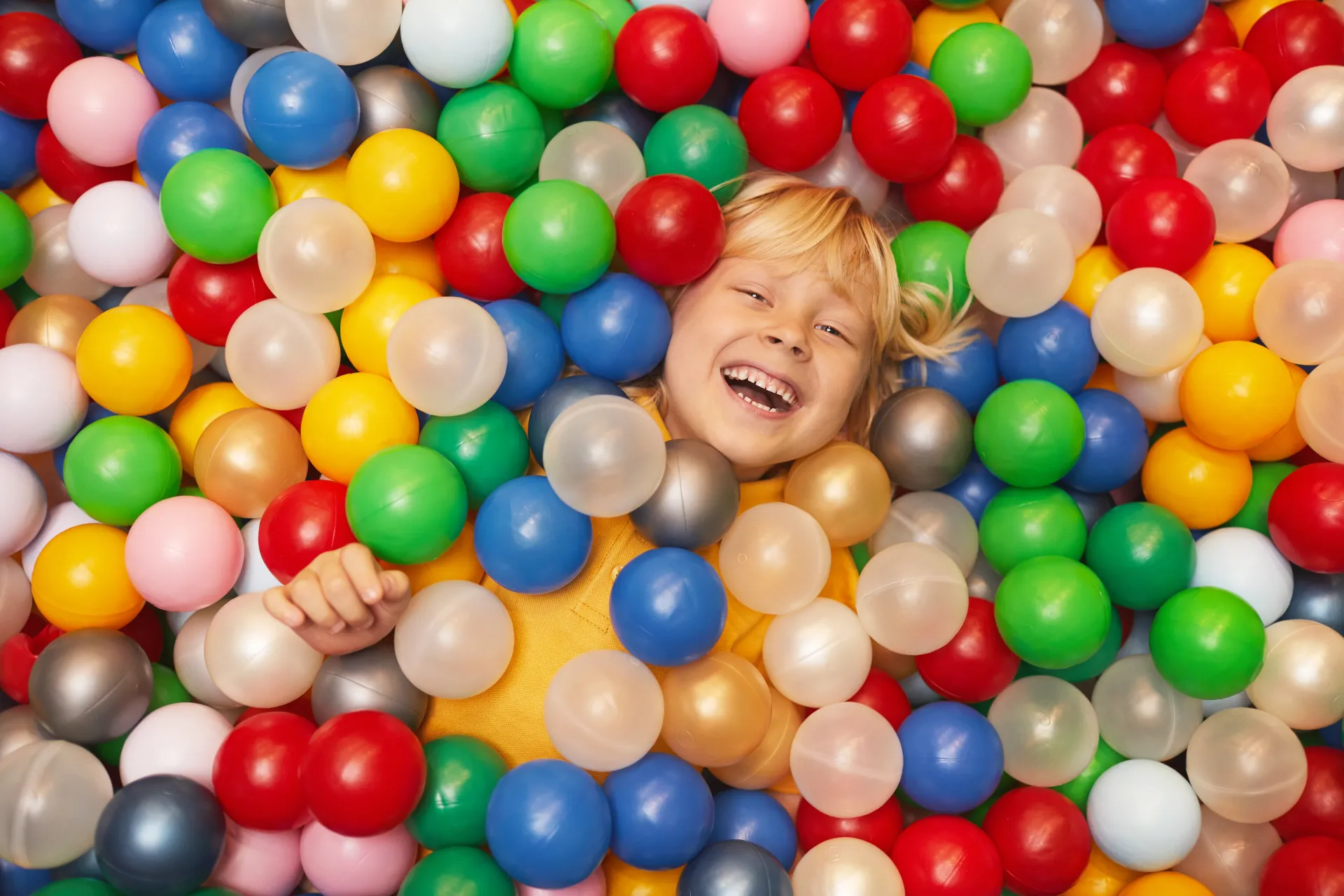 En liten jente ligger i en haug med fargerike plastkuler.