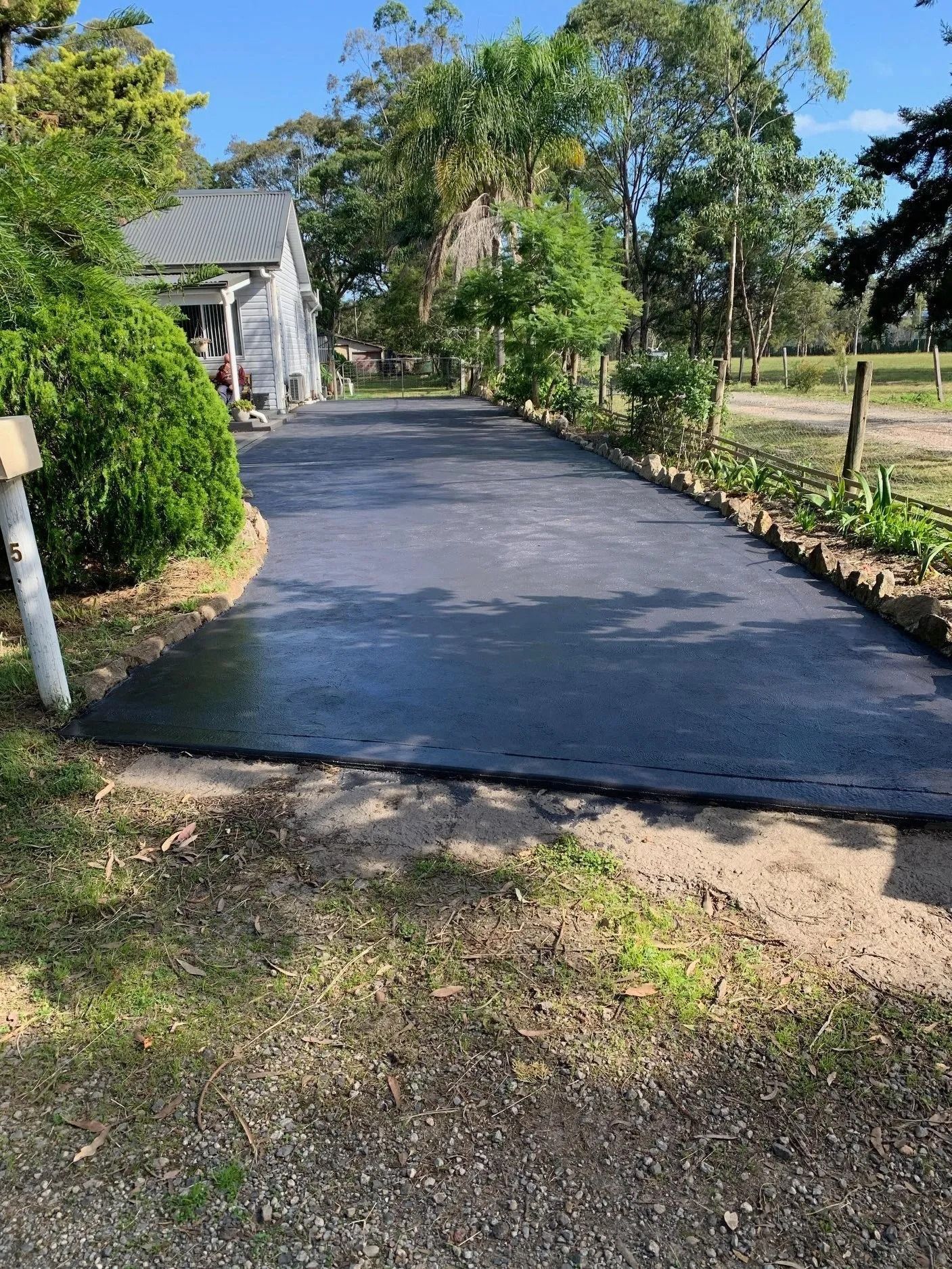Freshly paved black driveway curving through a green yard on a sunny day — BJ's Concreting in Shoalhaven, NSW