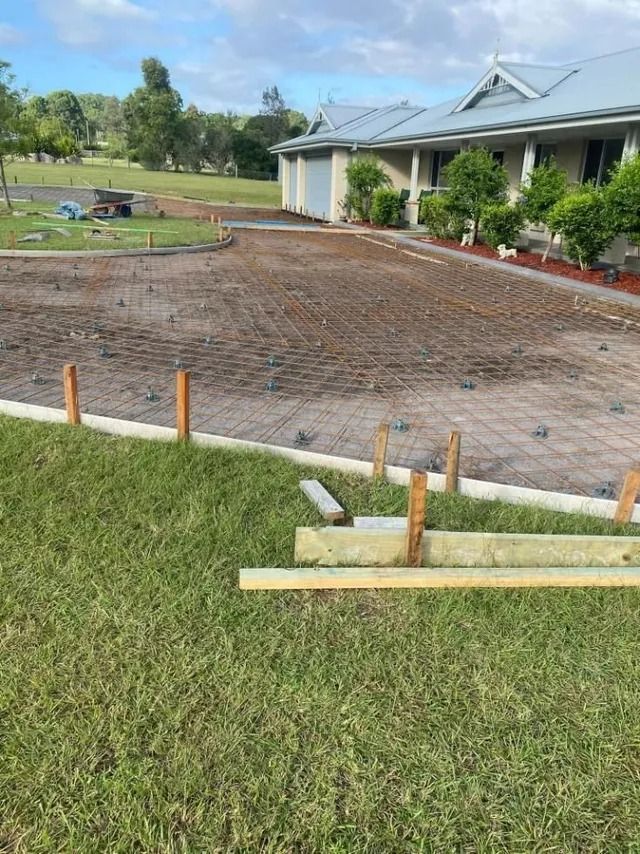 Freshly graded dirt area beside a house, with a grass foreground and survey stakes marking the edge. — BJ's Concreting in Shoalhaven, NSW