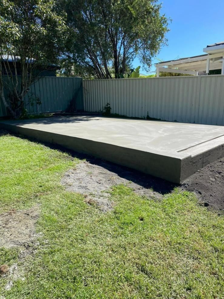 Concrete patio slab in a grassy backyard beside a corrugated metal fence and trees. — BJ's Concreting in Shoalhaven, NSW