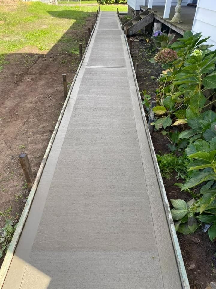 Concrete walkway ramp with metal edges beside a garden and soil path outdoors — BJ's Concreting in Bomaderry, NSW