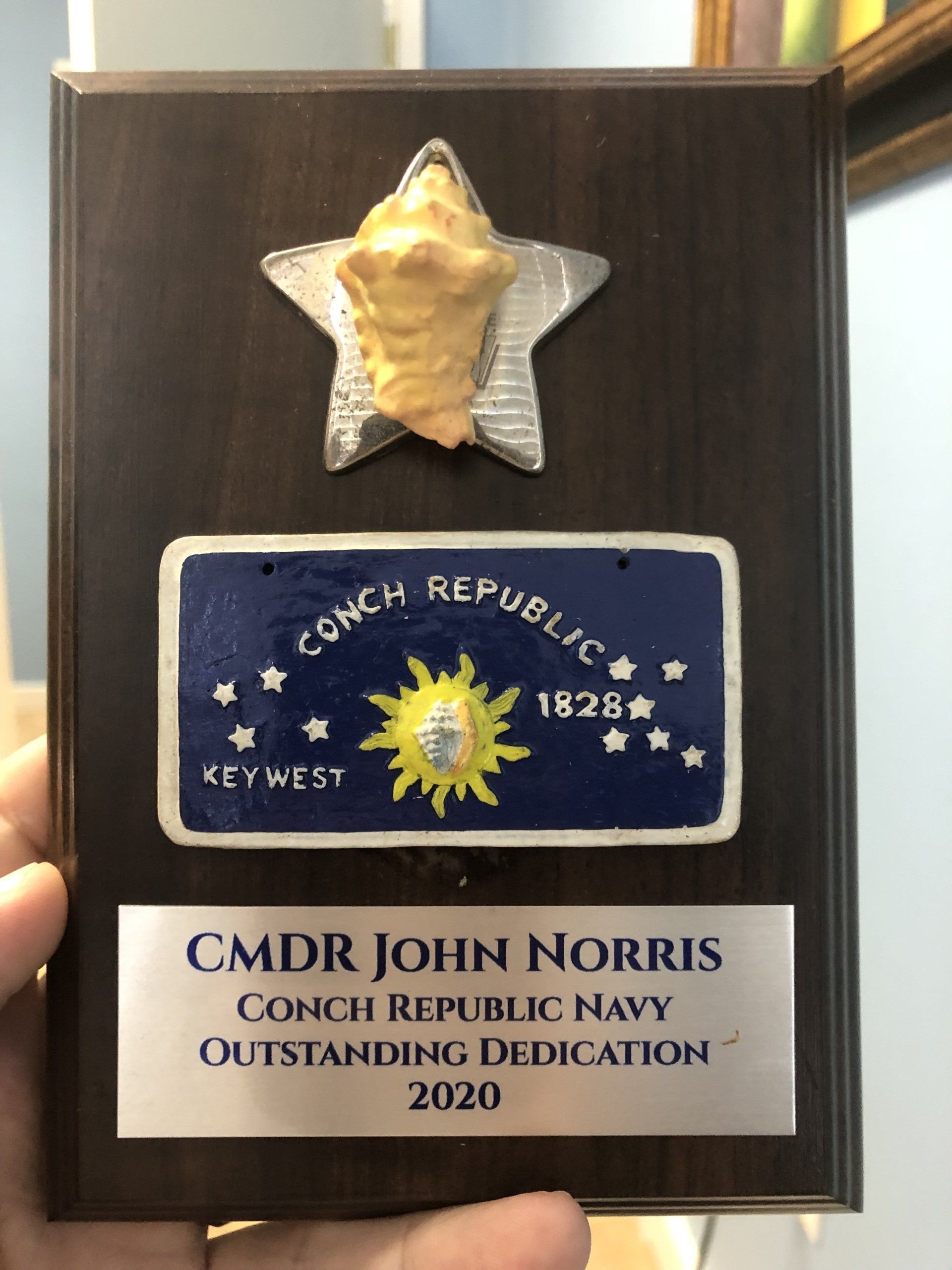 Plaque honoring CMDR John Norris: Conch Republic Navy award with conch shell and license plate design.