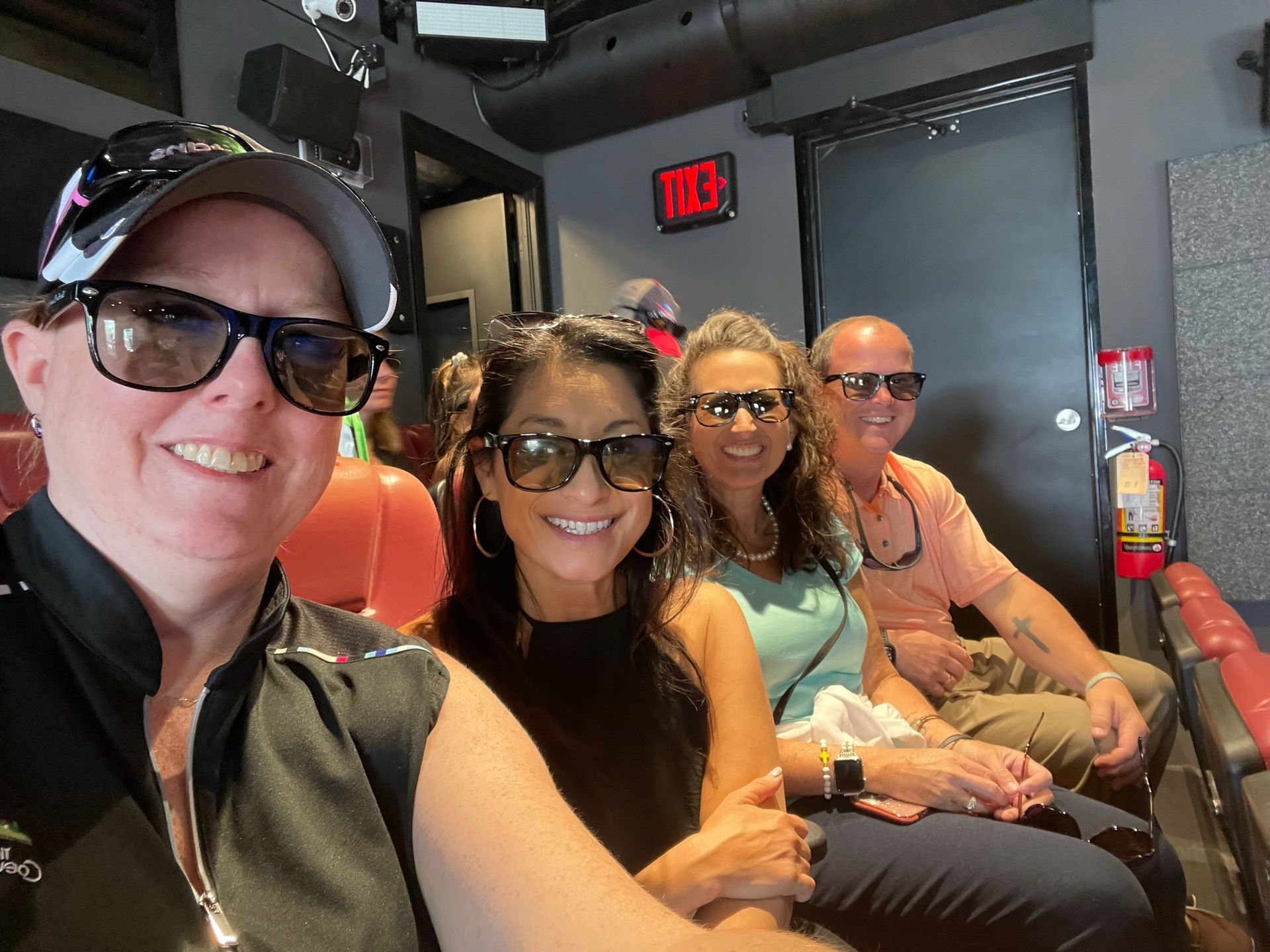 A group of people are sitting in a room with a red exit sign.