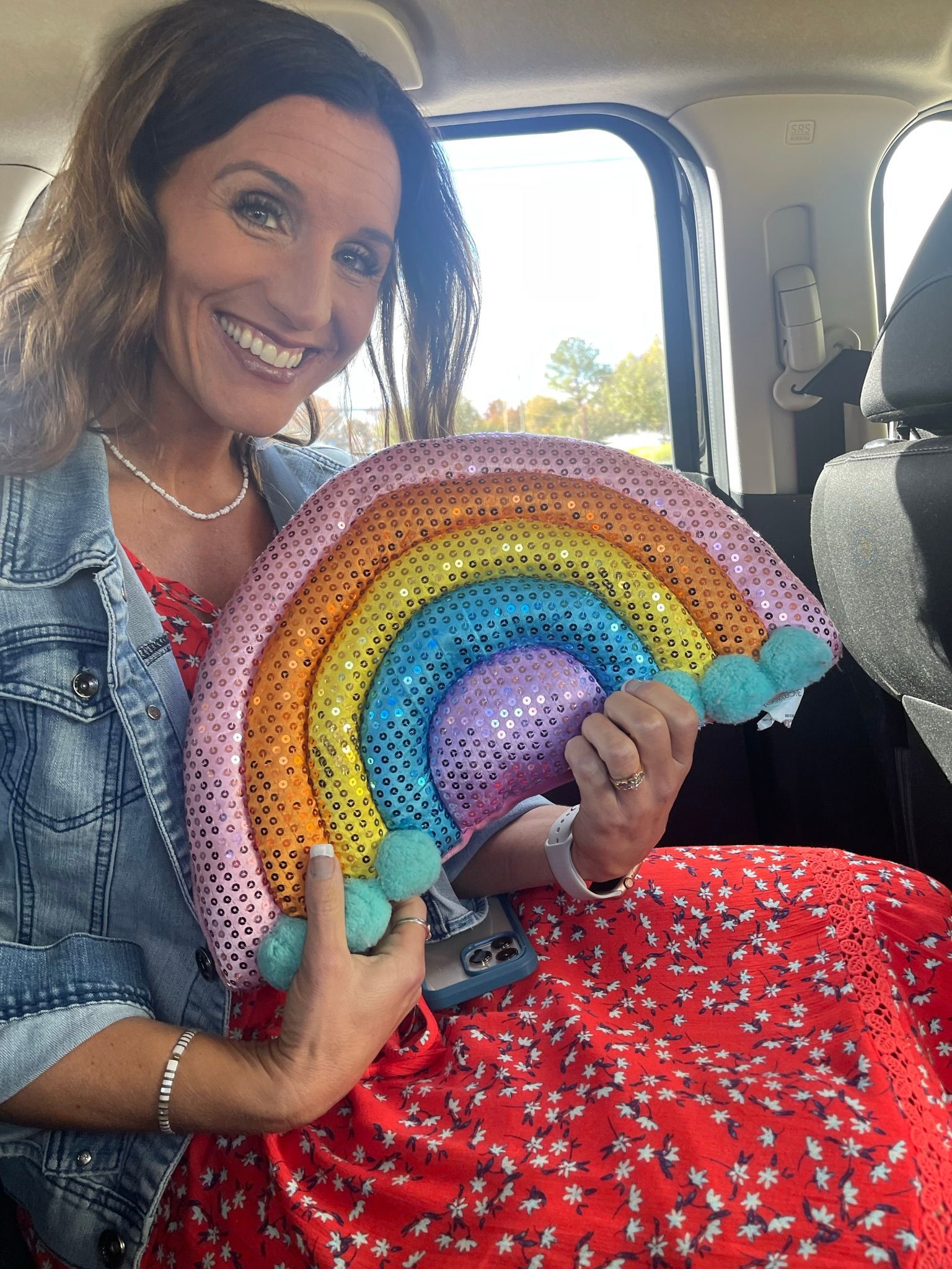 A woman is sitting in a car holding a rainbow balloon.