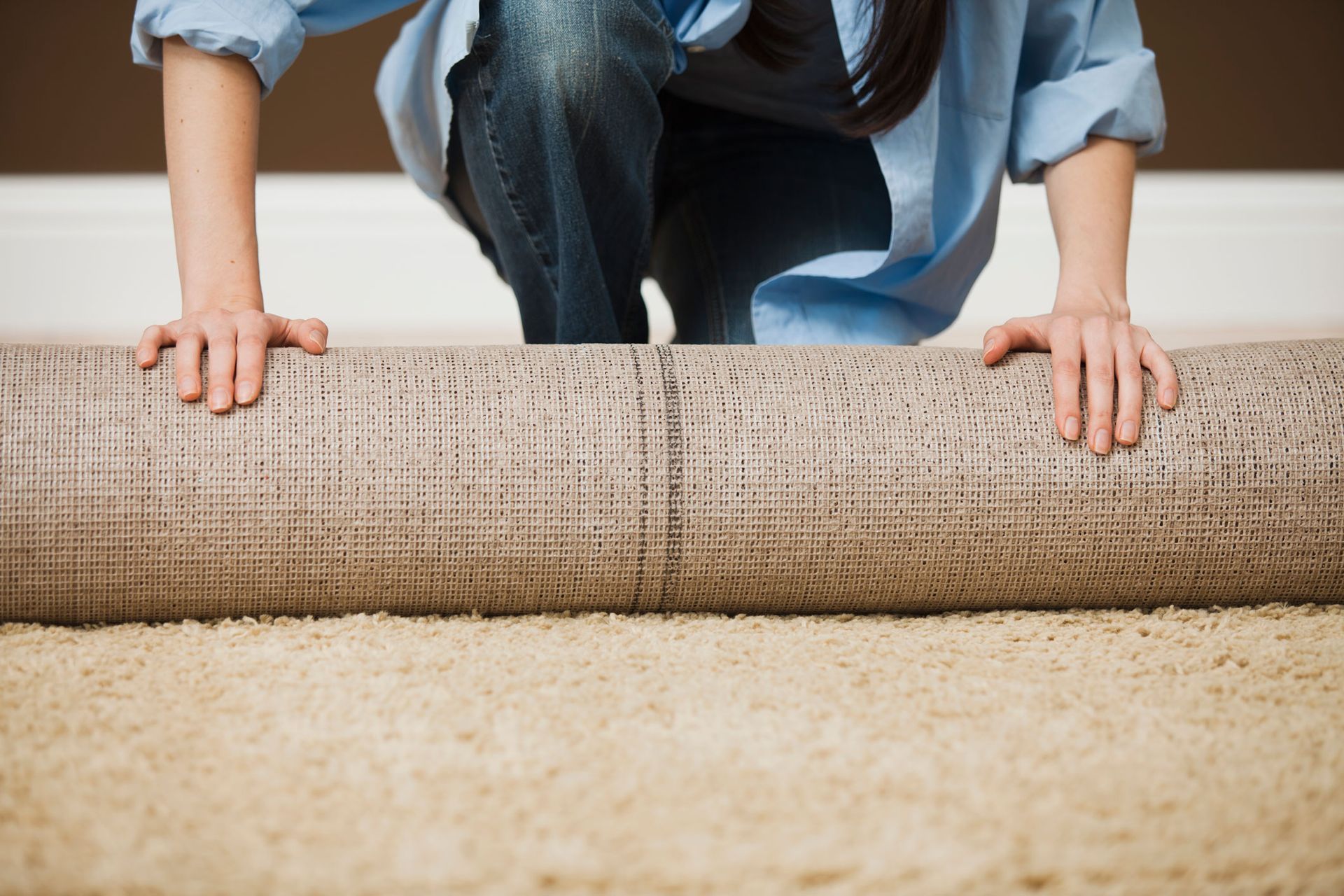 A woman is rolling a rug on the floor.