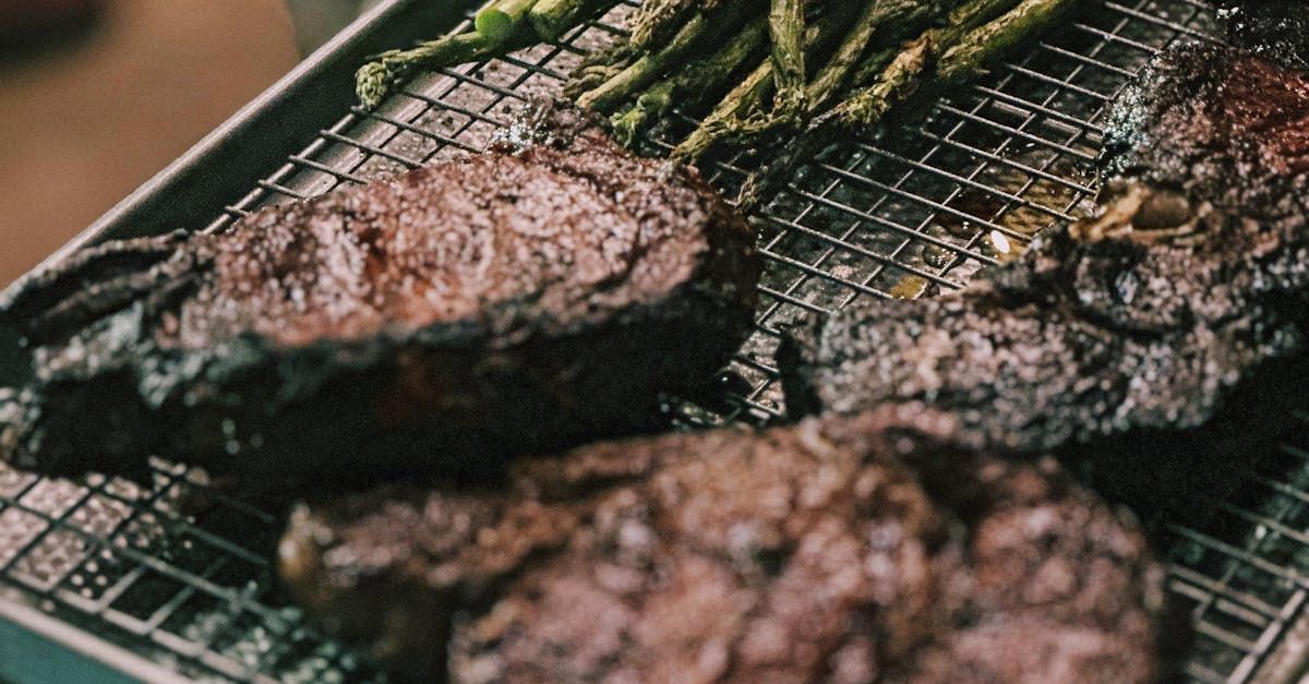 Two steaks and asparagus are cooking on a grill.