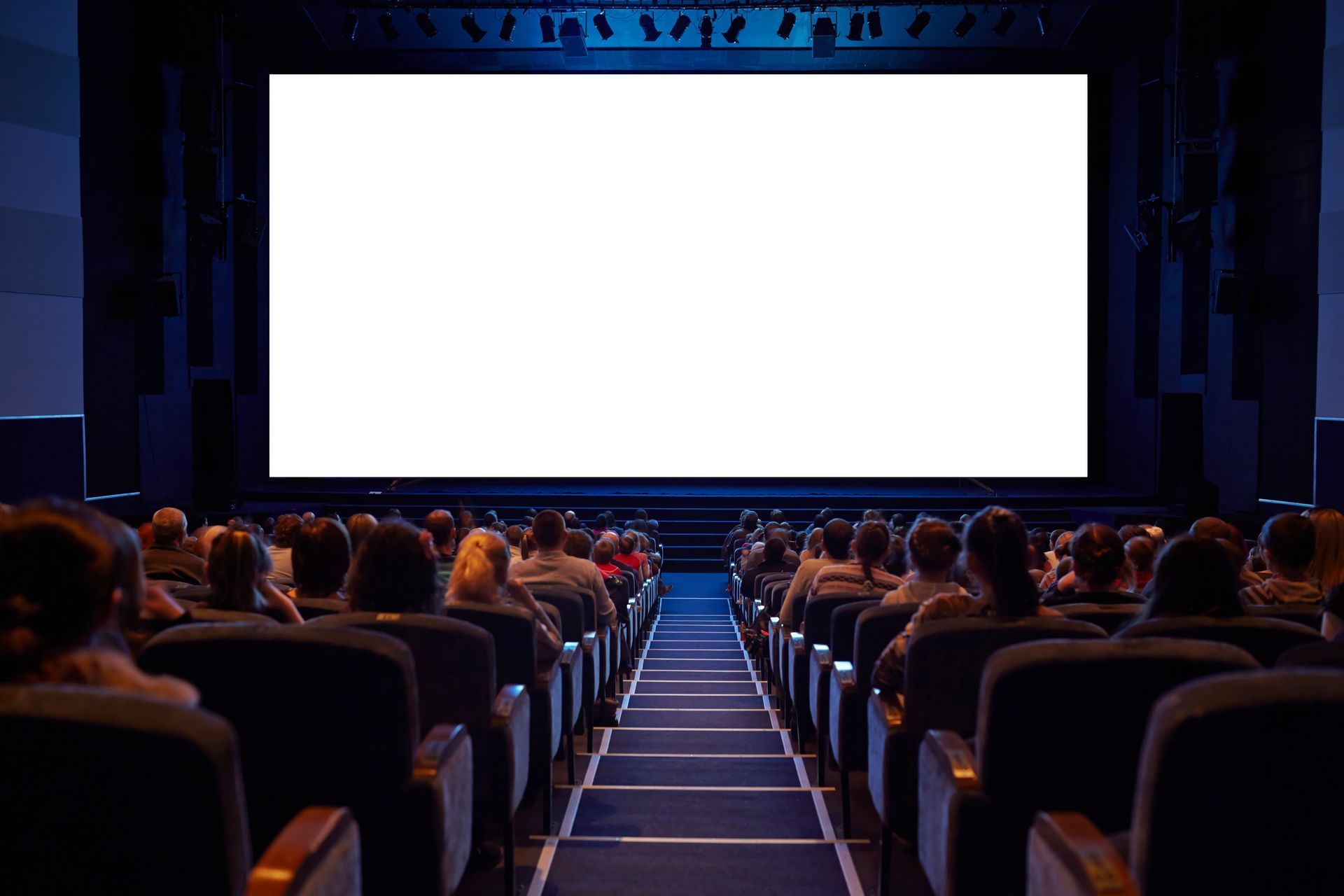 A view from the back of a movie theater looking toward a large, blank white screen above an audience seated in dark chairs.