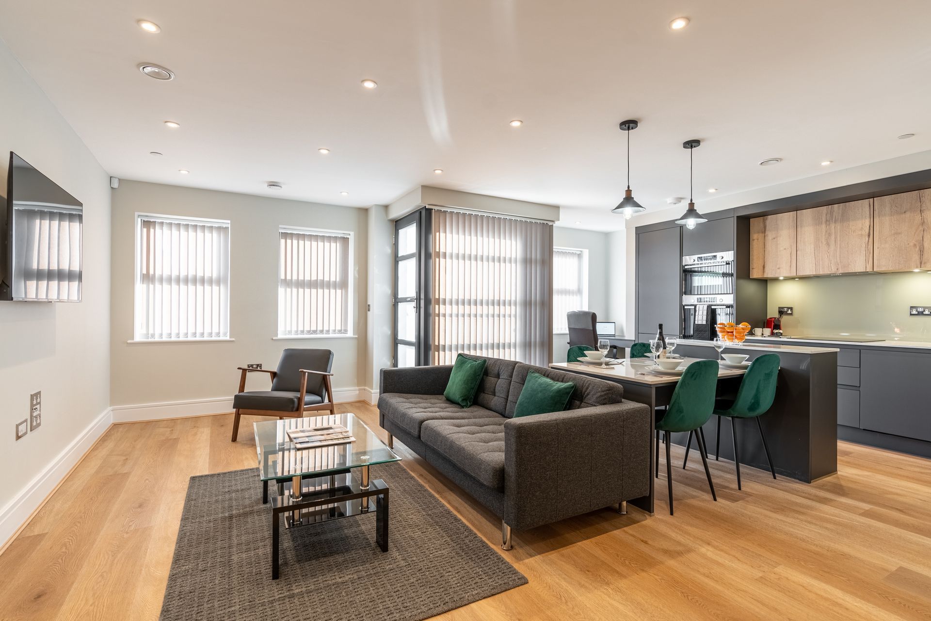 Modern apartment living room with sofa, kitchen, dining area, and wood flooring.