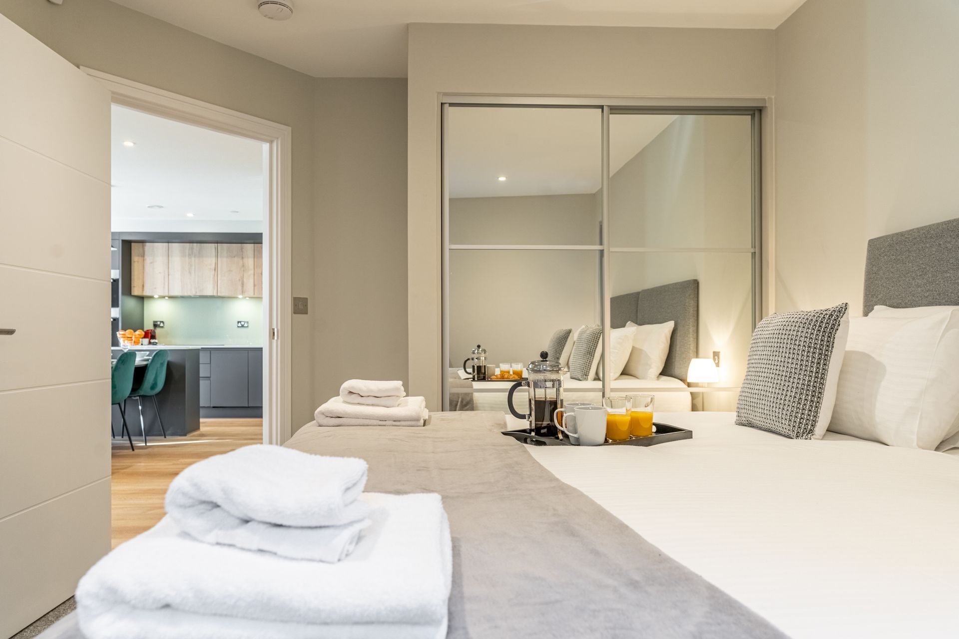 Modern bedroom with neatly made bed, folded towels, and a tray with coffee and orange juice.