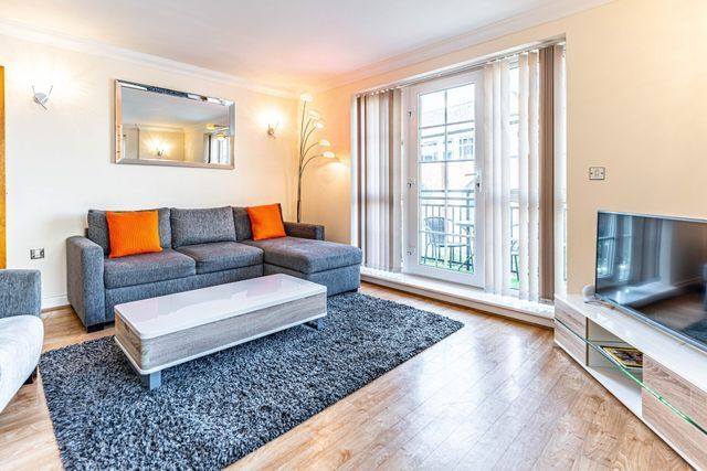 A modern living room with a grey sectional sofa, orange pillows, a rectangular coffee table, and a TV on a light wood unit.