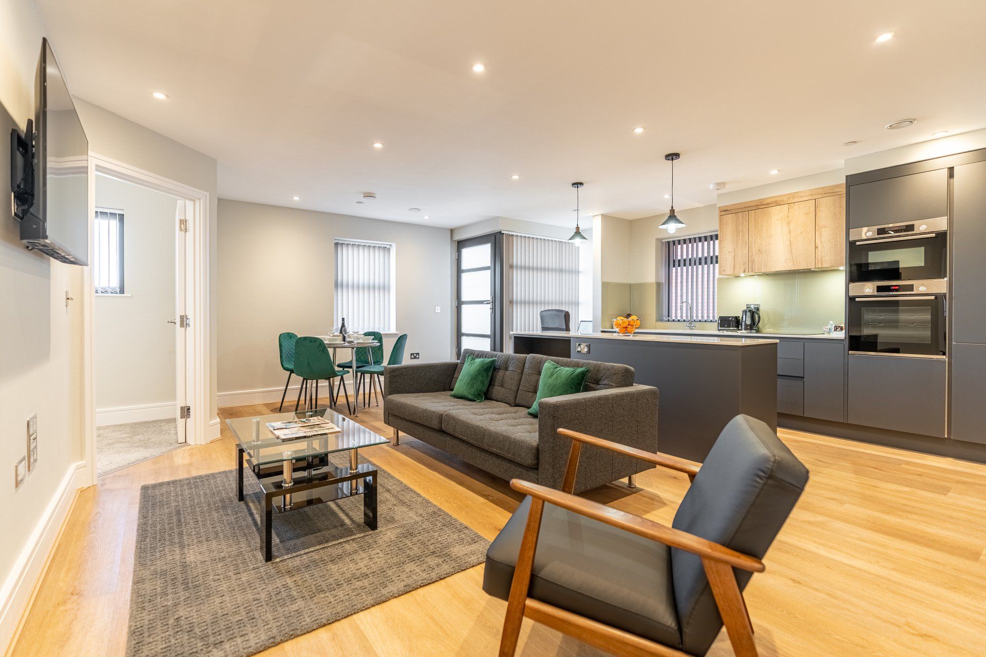 Modern open-plan living room and kitchen with wooden floors, dark sofa, and dining area.