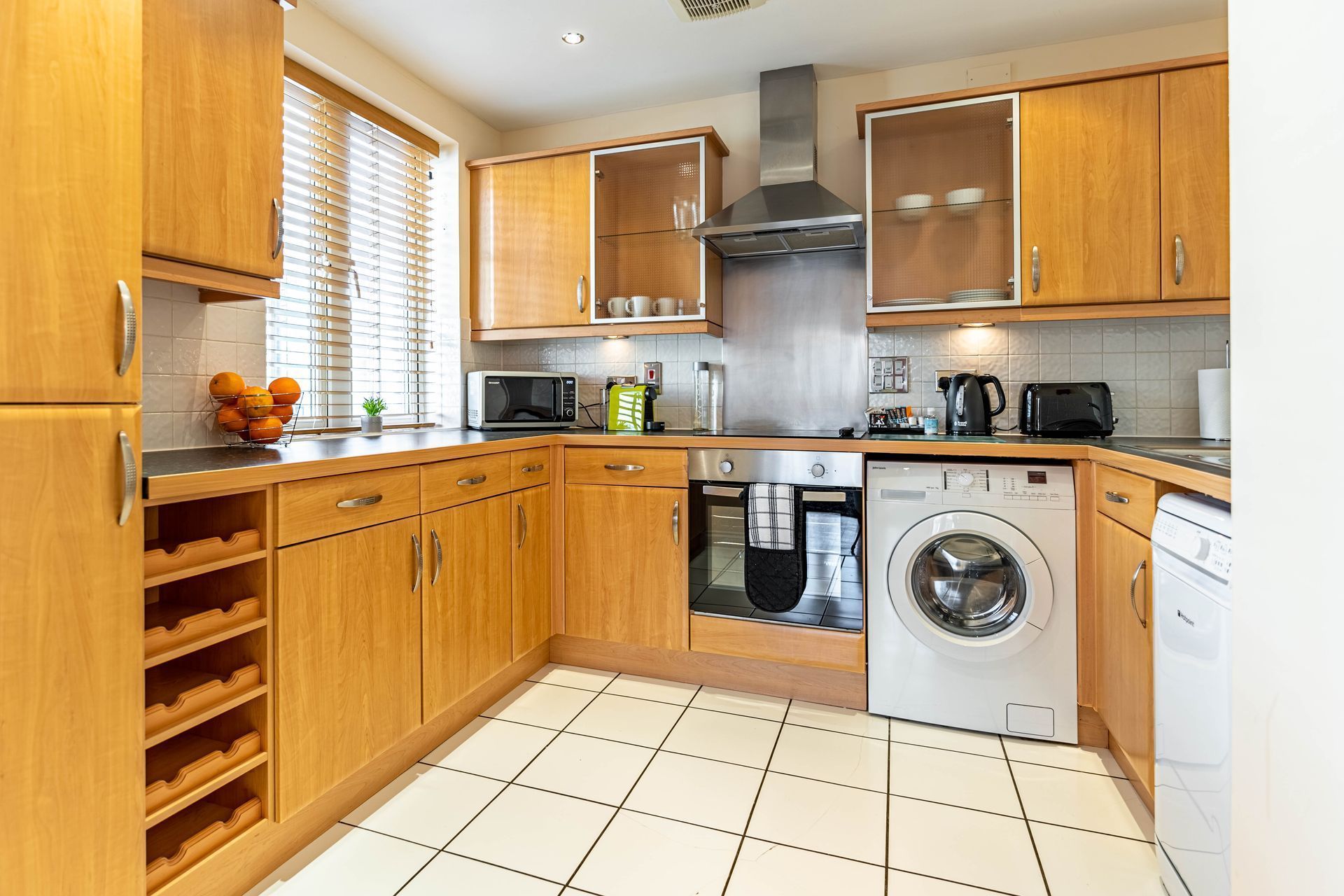 Modern kitchen with wooden cabinets, white appliances, tiled floor, and countertop essentials.