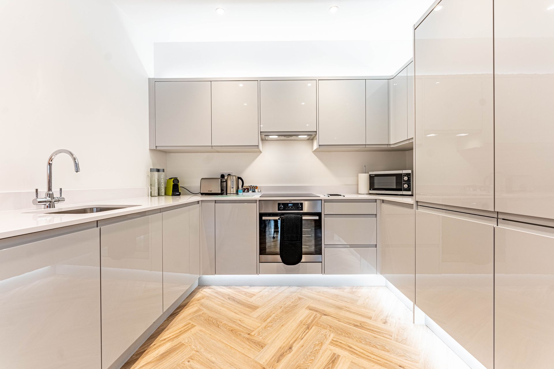 Modern kitchen with glossy cabinets, built-in appliances, and light wood herringbone flooring.