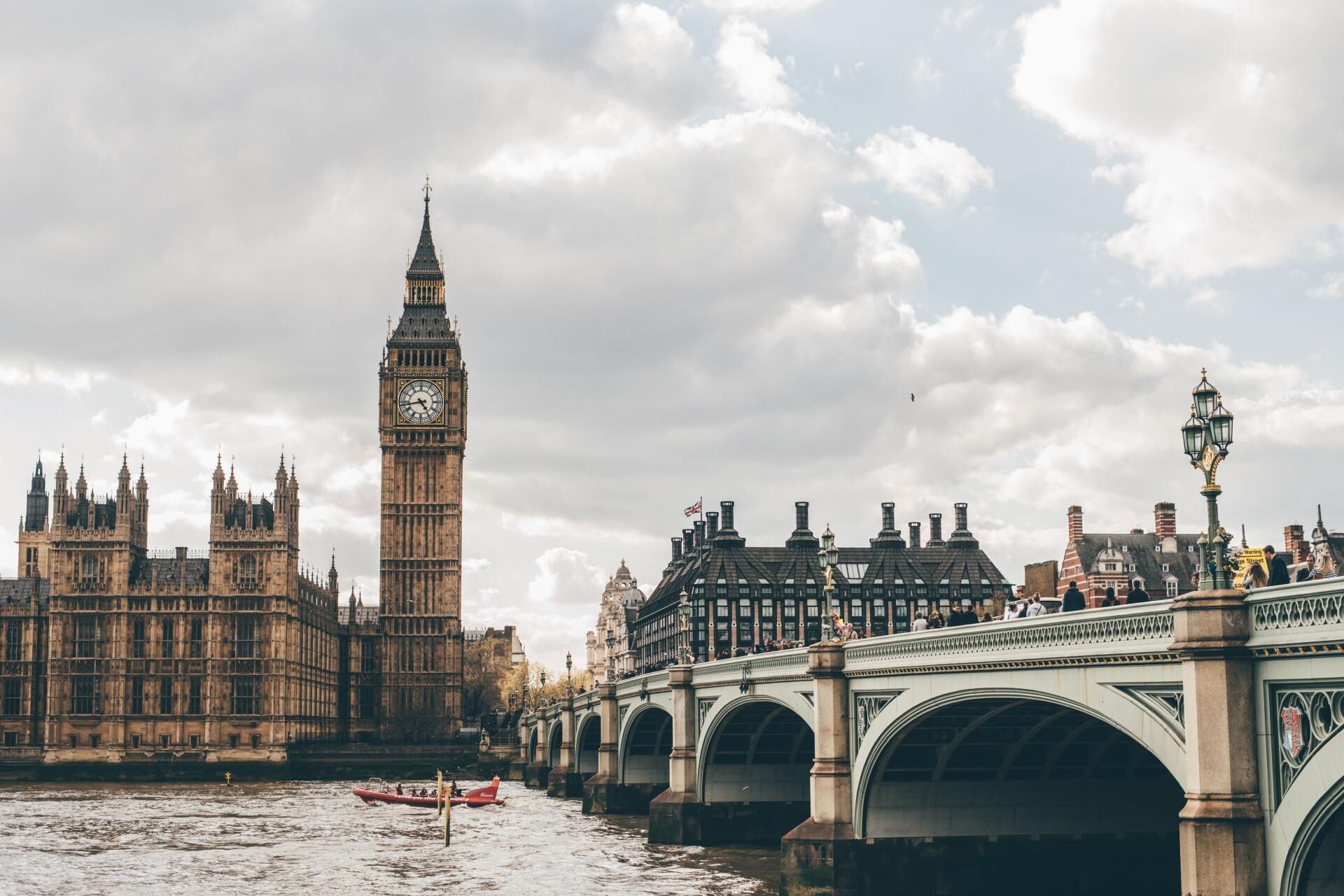 Big Ben and the Houses of Parliament tower over the Thames River near Westminster Bridge under a partly cloudy sky.