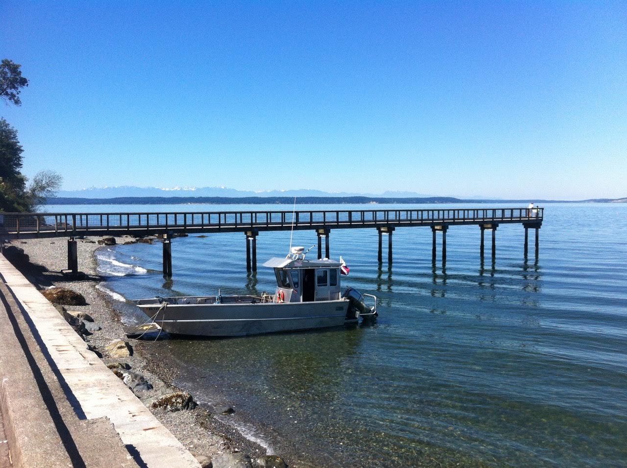 Small boat docked by a long pier over calm blue water on a sunny day