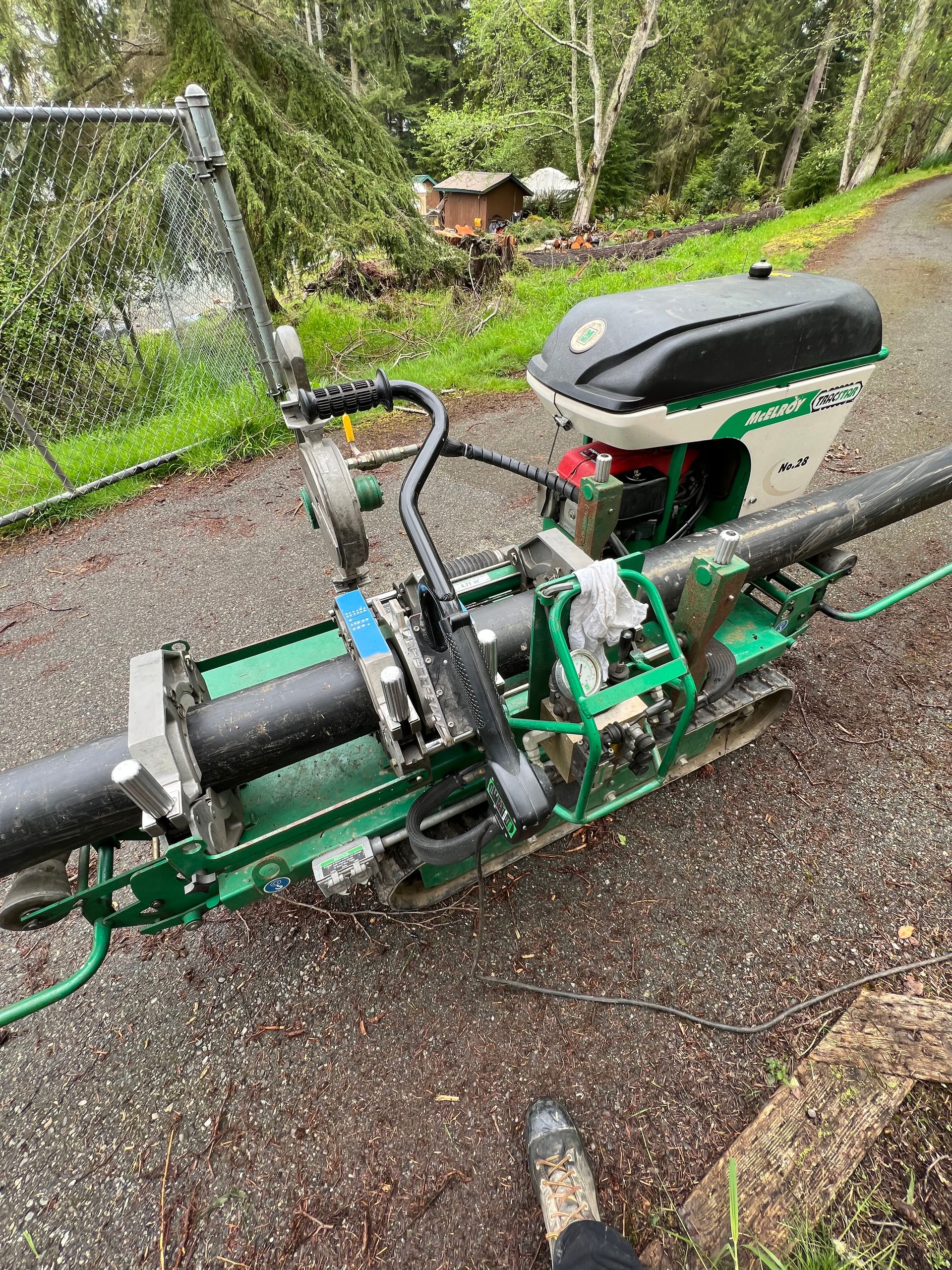 Green mountain bike lying on a wet gravel path beside a chain-link fence and garden