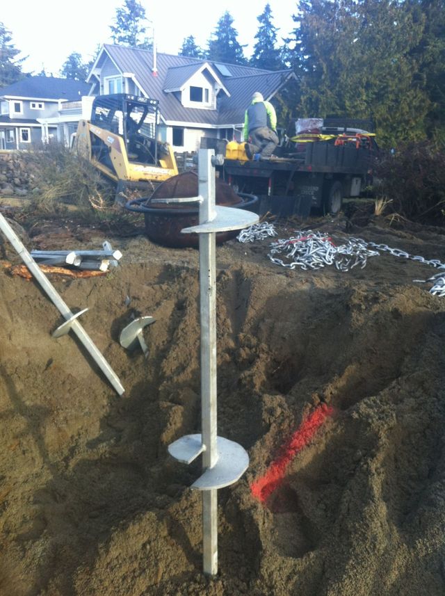 Construction site with a large excavation, steel post, excavator, and trucks in a residential neighborhood
