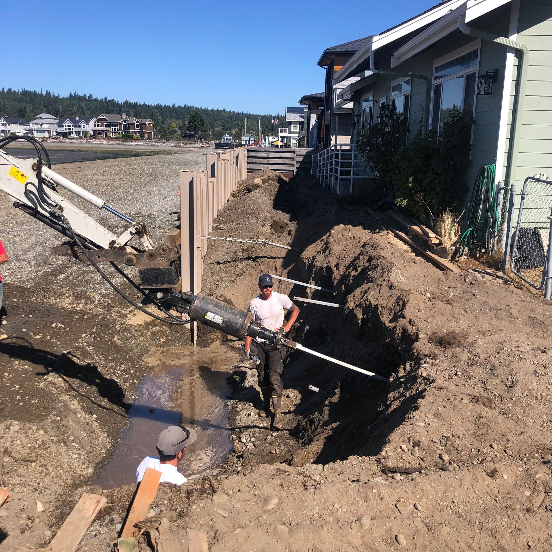 Workers digging a trench beside houses on a muddy construction site