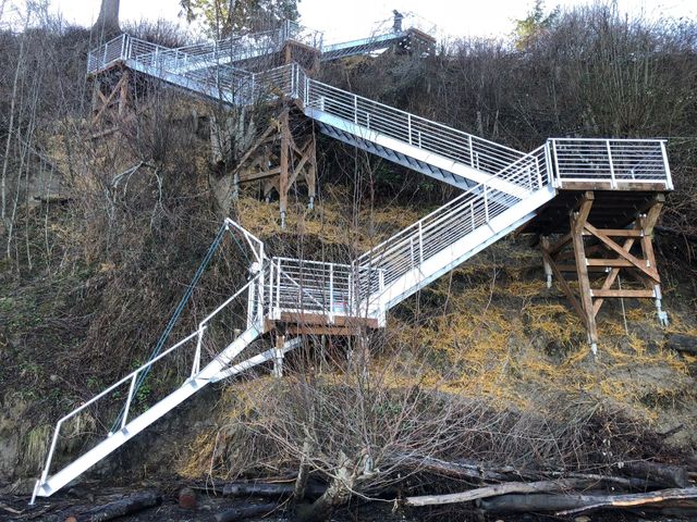 Stairway and wooden walkway zigzag up a steep, brush-covered hillside in a wooded area.
