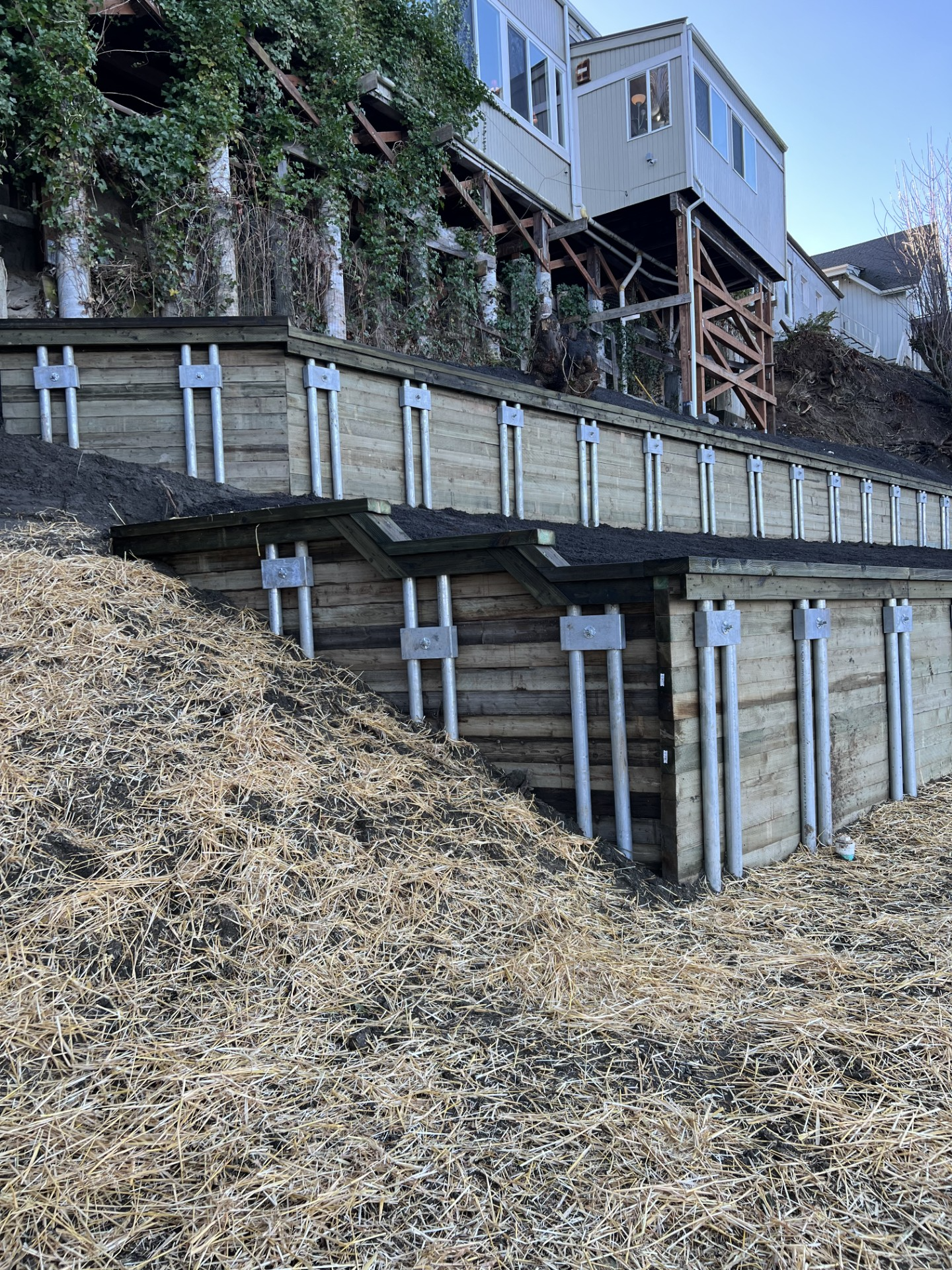 Retaining wall with wooden supports below a house on a steep, eroding hillside
