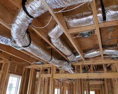 Unfinished house interior with exposed wooden framing and silver insulated HVAC ducts overhead.