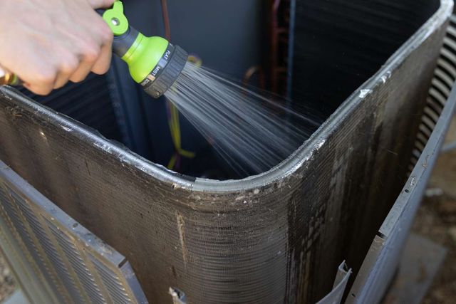 Hand rinsing a black metal container with a green hose sprayer