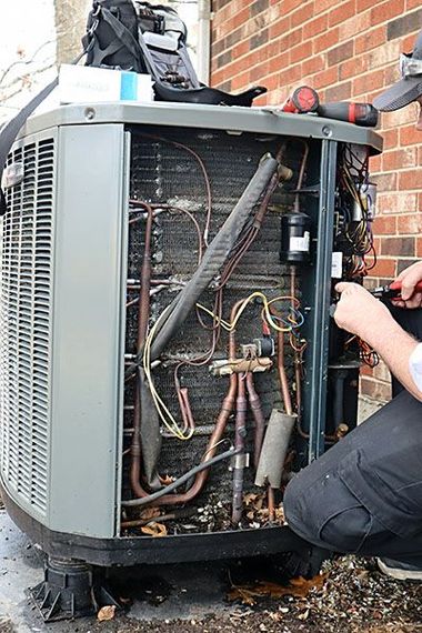 Open HVAC unit with exposed wiring and components; technician working beside a brick wall