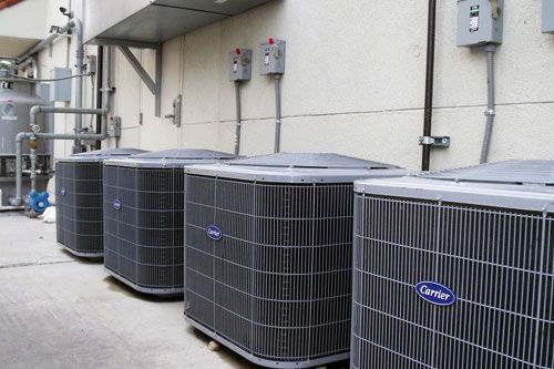 Row of large Carrier HVAC units beside a building wall and electrical boxes