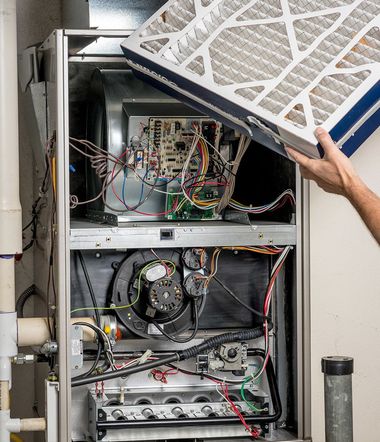 Open HVAC unit with a hand lifting the filter cover, exposing wires and internal components.
