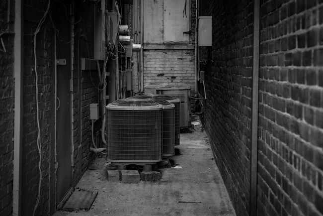 Narrow alley between brick walls with industrial units and vents at the end.