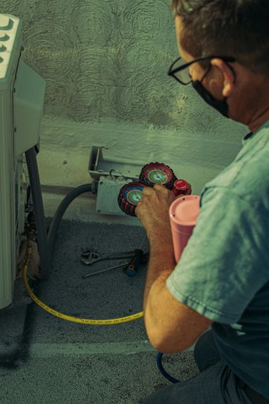 Worker in a workshop checks colorful gauges on a metal machine, holding a pink cup.