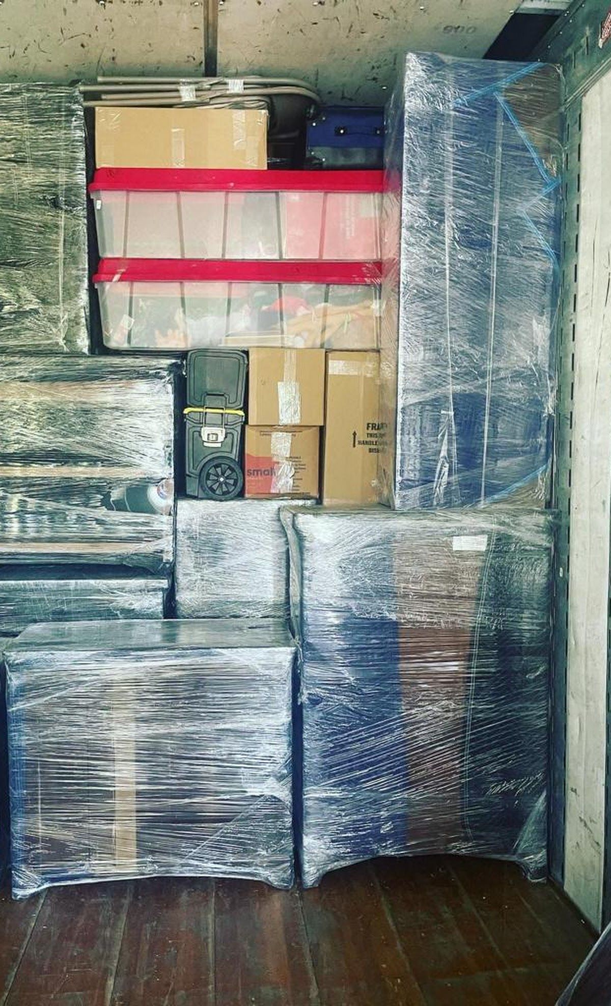 Furniture and boxes wrapped in plastic in a moving truck, stacked high. The truck's interior is visible.