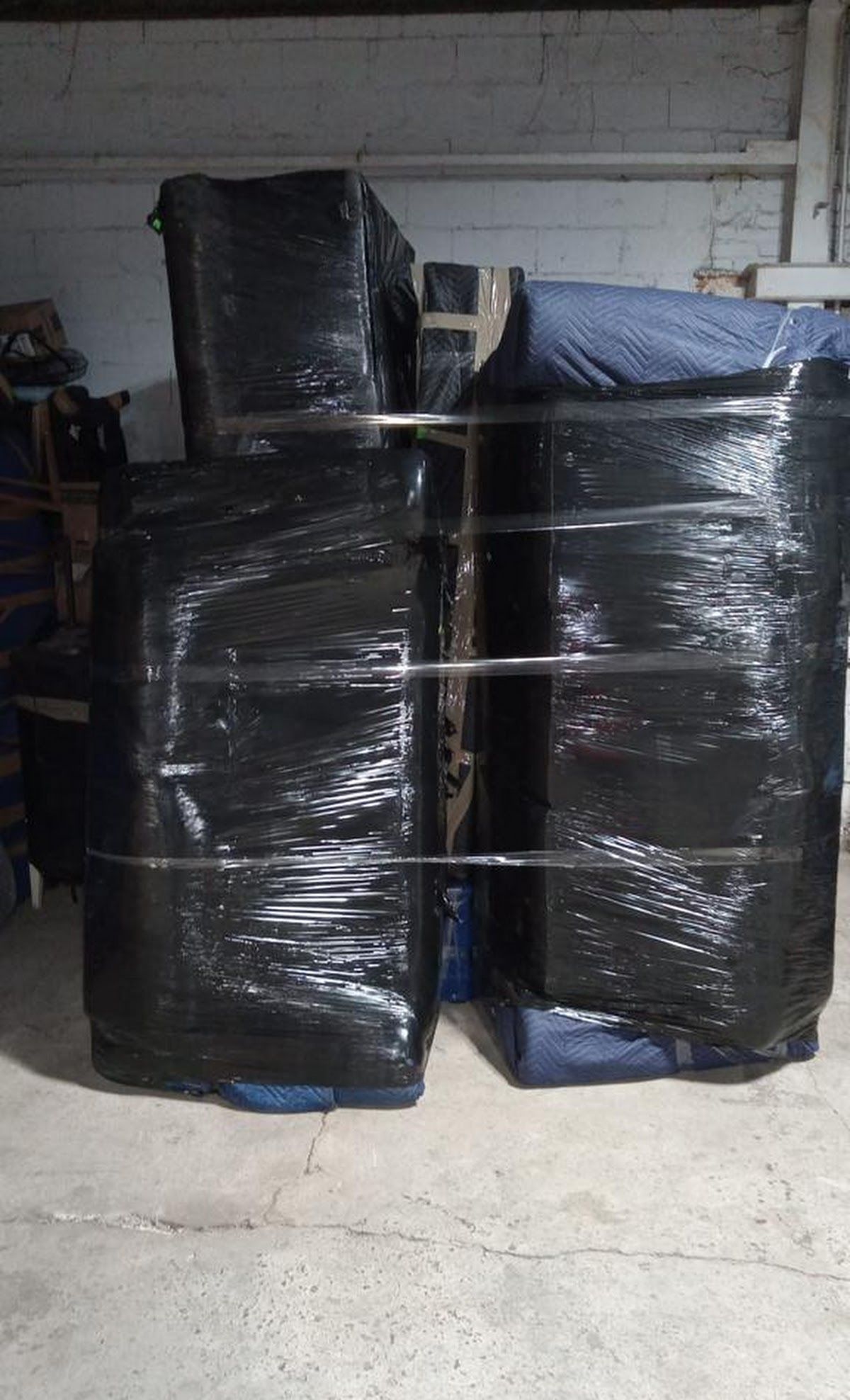 Wrapped furniture secured with metal bars, possibly for moving or storage, in a dimly lit warehouse.