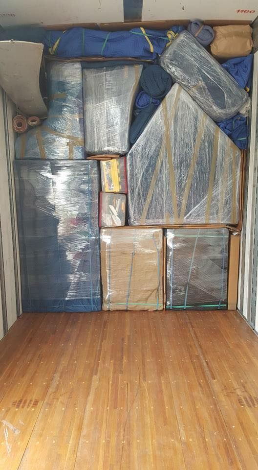 Boxes and furniture, wrapped in plastic and padding, are packed into a truck's wooden cargo area.